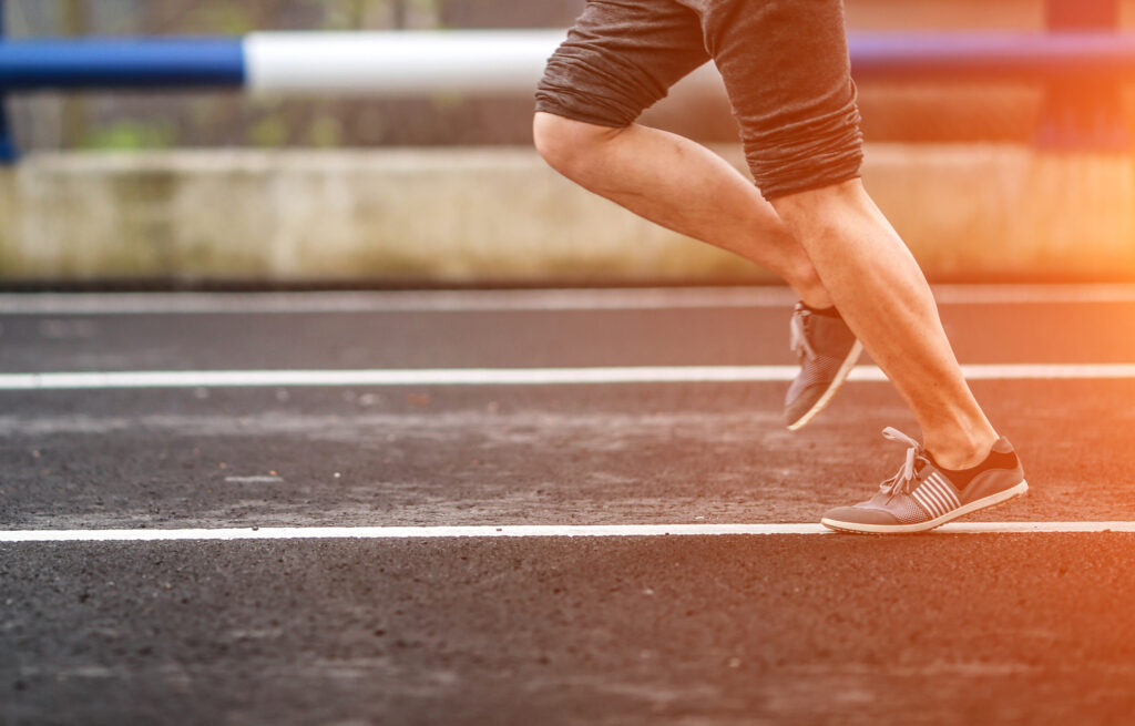 Close up of athlete's legs running on the empty road at the sunset