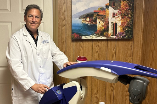 A photo of Dr. Waldman standing next to the Robotic M6 MLS Therapy Laser in his practice's treatment room.